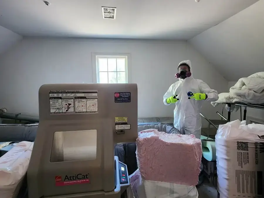 A crew member in a coverall and respirator working in a cleared attic space.