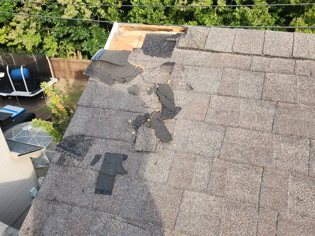 A hole torn clean through the roof decking at the edge of a shingled roof.