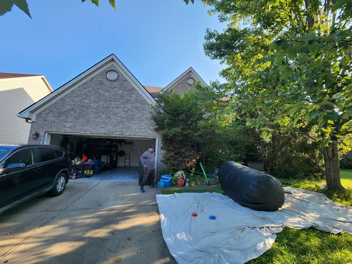 A driveway with the garage open and bagged insulation stacked on a tarp.