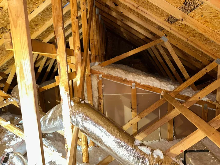An attic with clean new blown insulation across the joists and the duct runs wrapped.