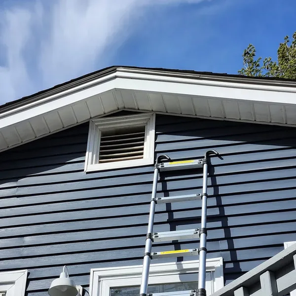A telescoping ladder set against a dark blue house reaching a second story gable vent.