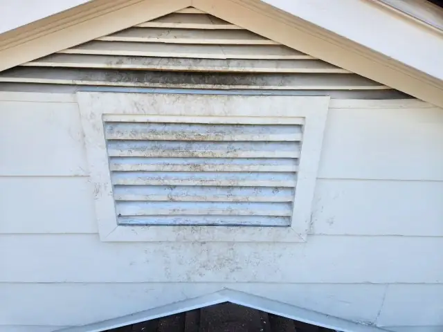 A weathered gable vent with mud and dirt streaked around the frame.
