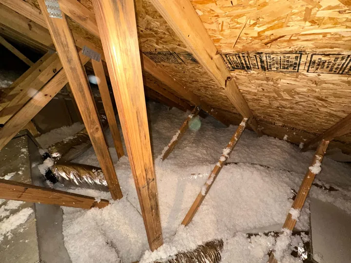 An attic after the work, clean new blown insulation across the joists with the ducts wrapped.