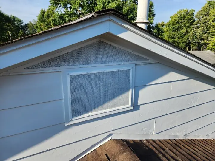 A finished gable vent with a bordered perforated metal guard installed and painted to match the siding.