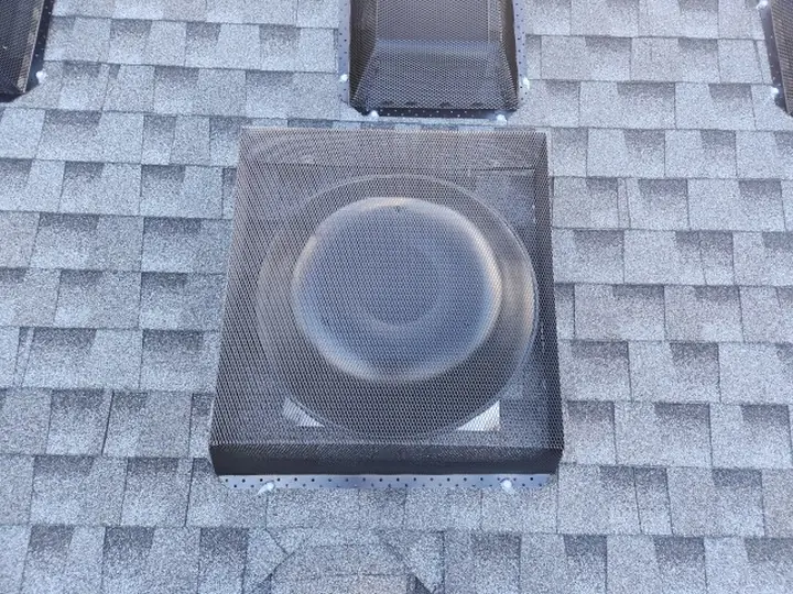 A roof vent covered with a perforated metal guard, with a second guarded vent behind it.
