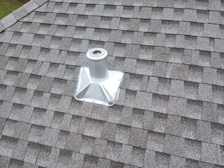A plumbing vent stack on a shingled roof with new metal flashing fitted around its base.