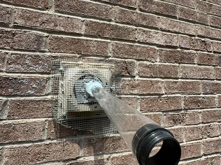 A one way bat tube fitted over a bathroom fan vent on a brick wall.