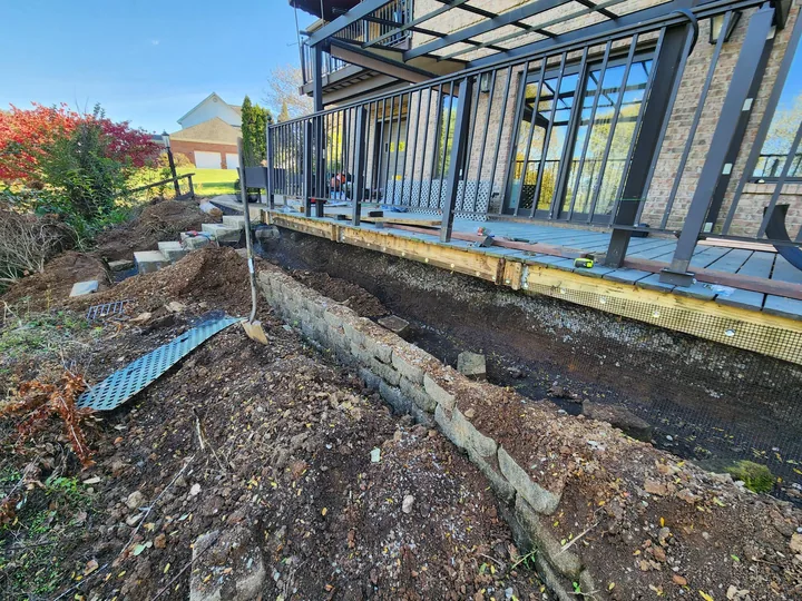 A trench dug open along the foundation of a sunroom with mesh being laid in.