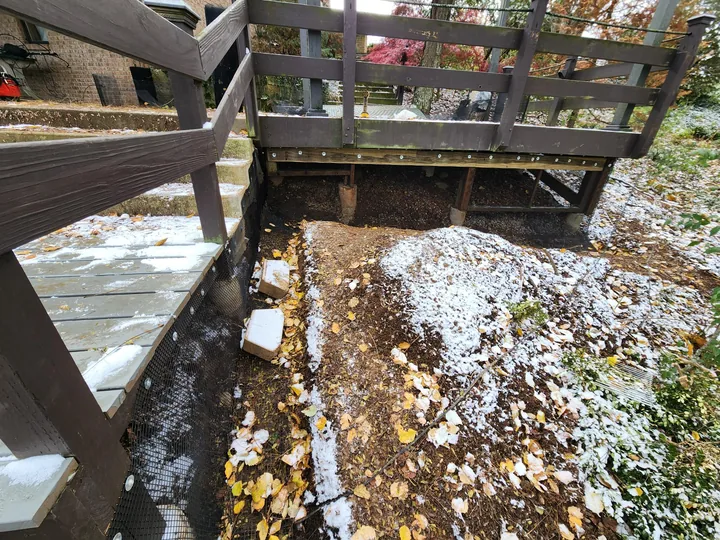 A finished dig barrier along the edge of a wooden deck with snow on the ground.
